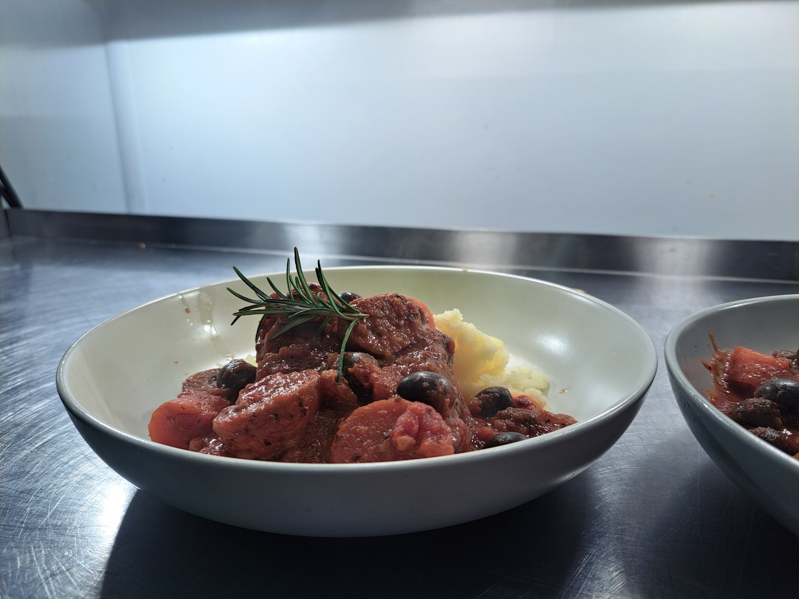 A slow-cooked beef dish finished with rosemary, plated in the kitchen